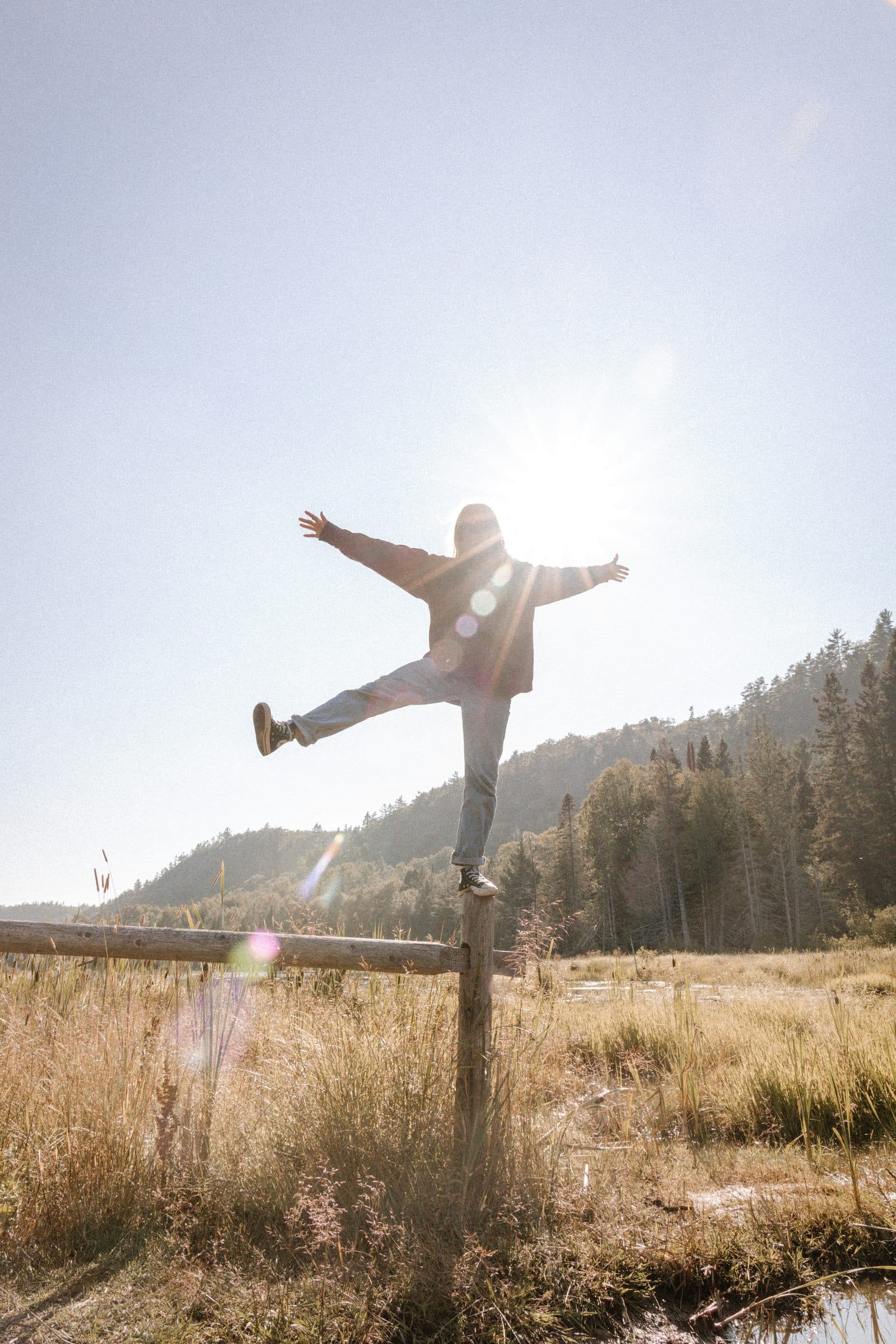 A person balancing on a fence post, arms outstretched against the sun